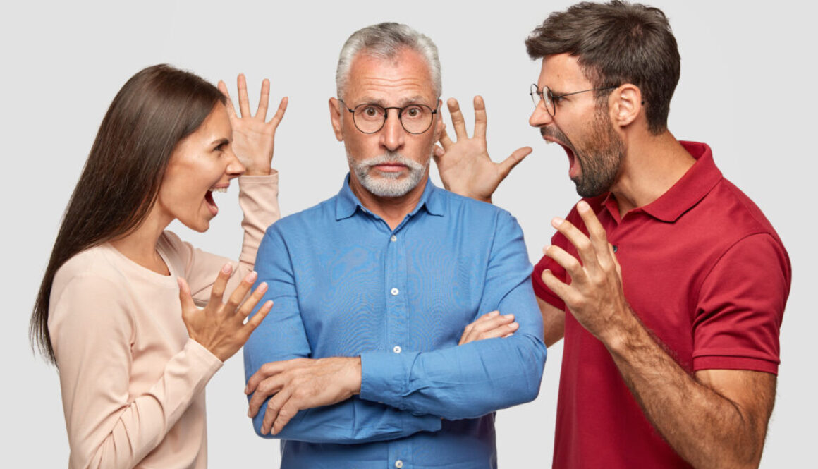 Guilty grey haired bearded senior man keeps arms folded, hears approaches from young colleagues who shout angrily at him. Annoyed woman and man yell at mature father, sort out family relationships